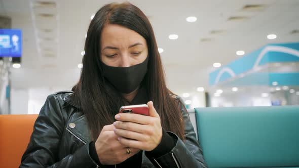 A Young Beautiful Girl Sits in the Airport Waiting Room and Uses a Mobile Phone. Woman Buying E alt