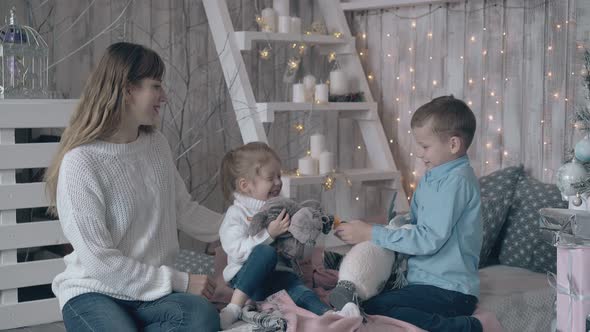 Mother in Sweater Watches Son and Daughter Play with Toys alt