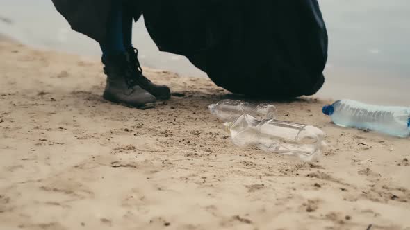 Volunteer collects empty plastic bottles scattered on the seashore, environmental pollution.