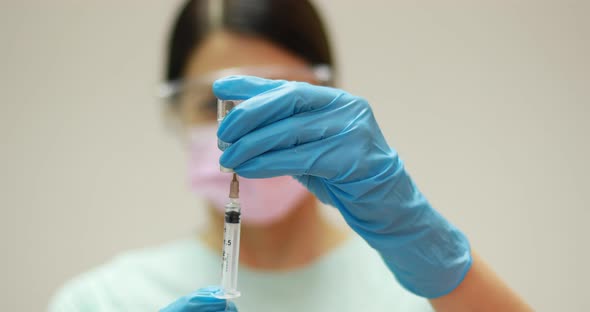 Doctor scientist protective gloves and mask holding glass vial with injection liquid. Vaccination