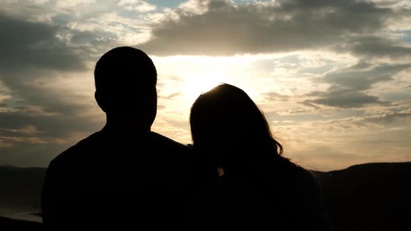 Silhouettes of a Young Couple at Sunset. A Woman Puts Her Head on Her Boyfriend's Shoulder.