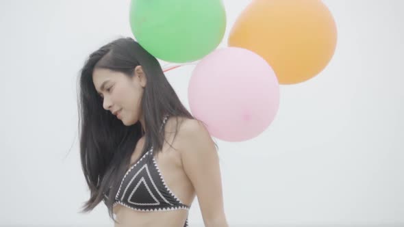 Beautiful young asian woman in bikini sexy holding balloon walking on beach. alt