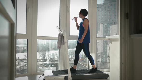 Athletic female is drinking water during exercising on treadmill. alt