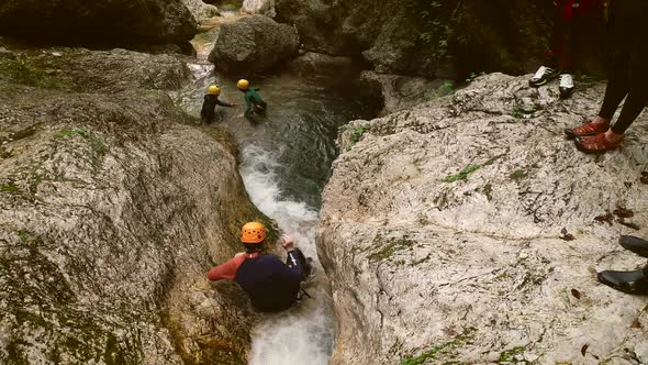 Aerial view of a group of people canyoning and sliding through rocks in river. alt