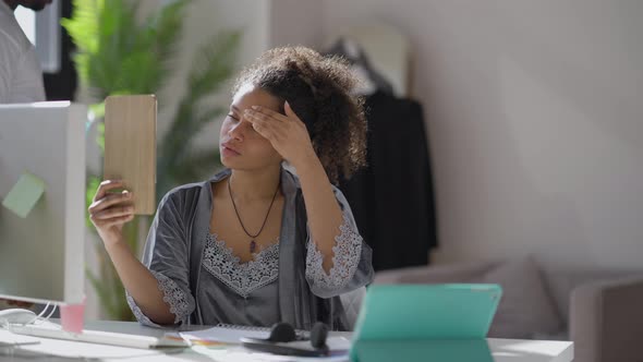 Young African American Woman Looking in Mirror in the Morning As Man Passing at Background Sitting alt