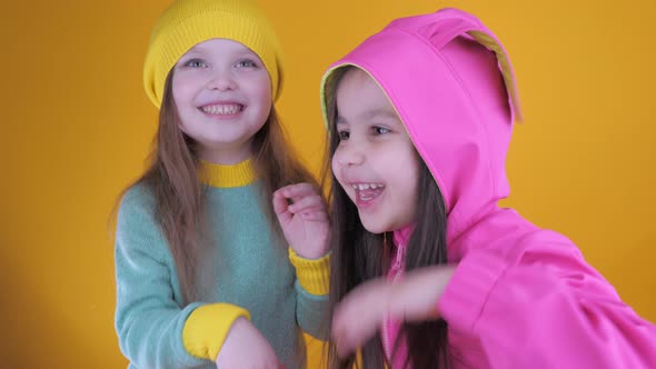 Two Cheerful Cute Little Girls Having Fun on a Yellow Background alt