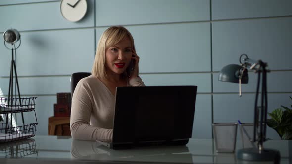 Businesswoman Is Talking By Mobile Phone and Working with Laptop in Office Room alt