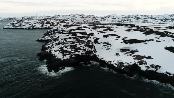 Waves of the Arctic Ocean Beat Against a Rocky Shore Covered with Snow