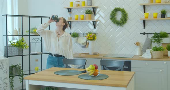 Happy Young Woman Dancing in Kitchen in the Morning Listening To Music on Smartphone and Coffee at alt