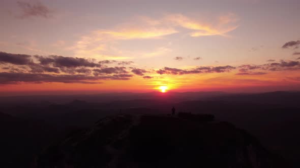 Person Standing on Rock with Epic Mountain Viewpoint with a Sunset Drone Aerial Landscape Shot