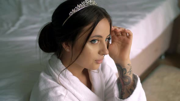 Attractive young girl with a tattoo on her arm in a white robe in the bedroom in the morning