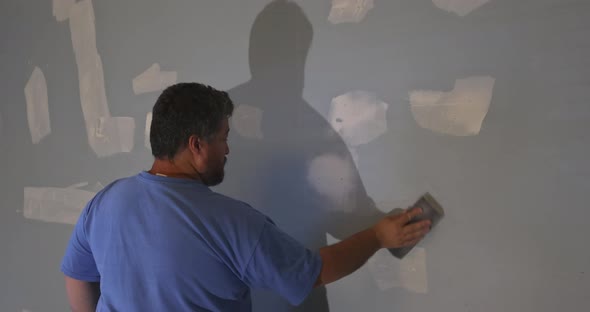 Worker Sanding the Drywall Mud Using Sand Trowel During Renovation the House alt