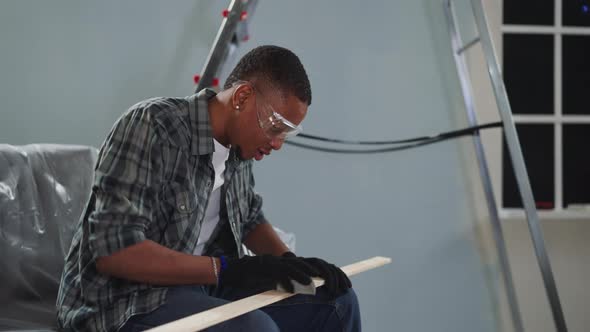 Young Black Worker with Goggles Polishes Wooden Plank alt