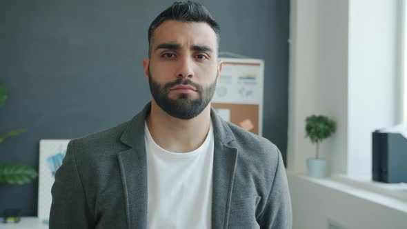 Middle Aged Businessman in Trendy Clothing Standing Indoors in Office Looking at Camera with Serious alt