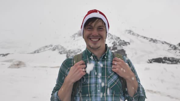A Snowball Flies Into the Face of a Funny Guy in a Christmas Hat on the Background of Mountains alt