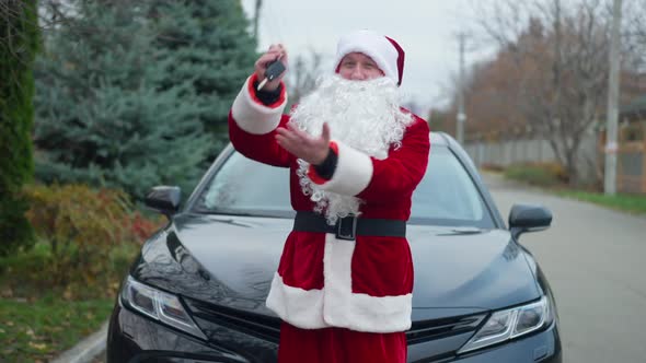 Positive Cheerful Santa Clause Bragging Car Keys Standing at Vehicle Outdoors Looking at Camera alt
