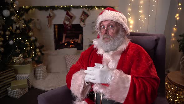 Portrait of Funny Santa Claus in Glasses, Sitting in His Rocking Chair Near the Christmas Tree and