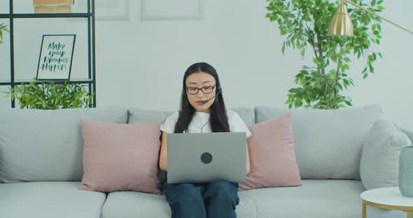 Asian Woman in Glasses Sit on Couch Wear Headset Use Laptop Having Distant Communication alt