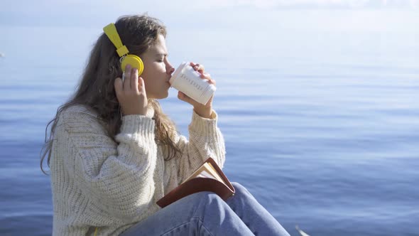 Woman in Sweater Takes Cup of Coffee on Seashore