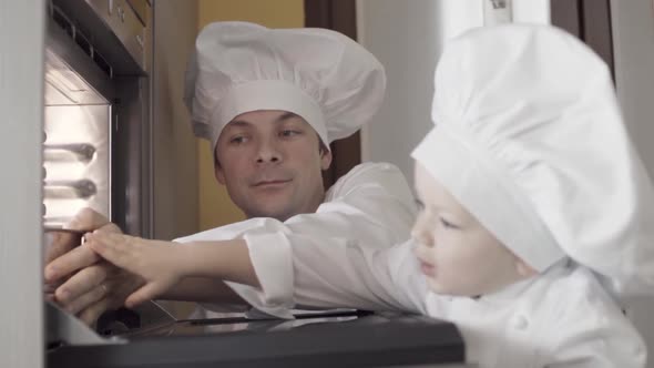 Slow Motion of Young Child Chef Puts Cake in and Electric Oven with His Dadwatch and Waitin the alt