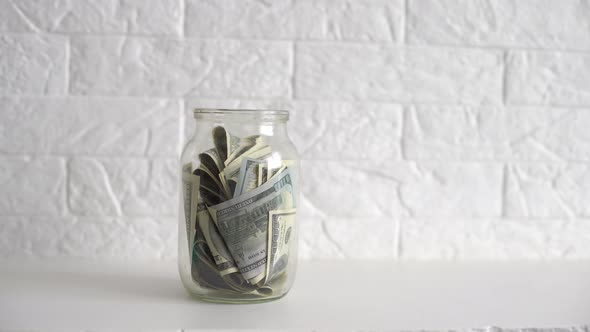 Hand Putting a Dollar Bill in a Savings Jar with a White Label alt