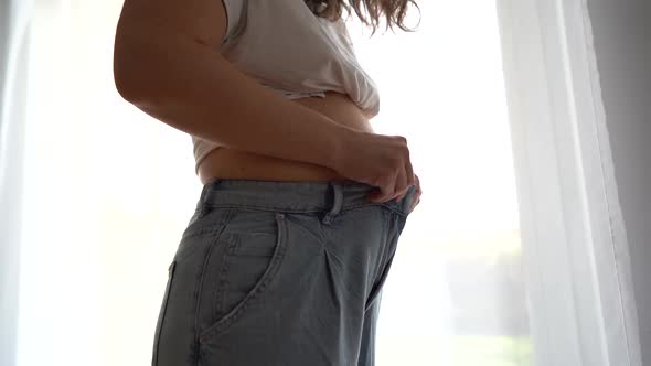 Closeup of a Young Woman Touching Her Belly Trying To Button Up Tight Jeans alt