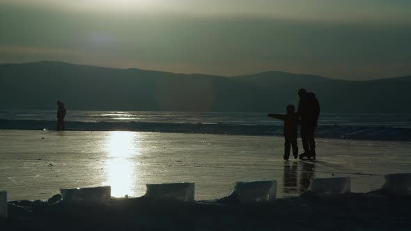 Father and Son Go Ice Skating on Frozen Lake at Sunset in Winter