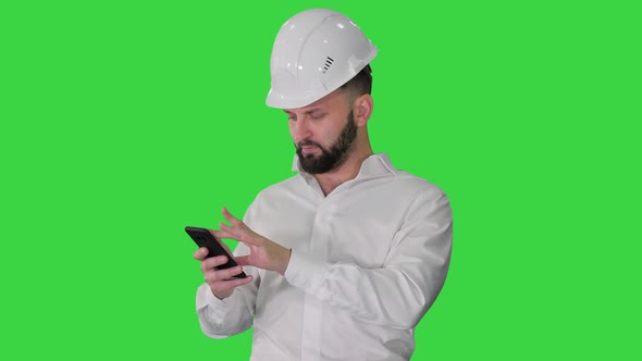 Smart Engineer in White Shirt and Safety Engineering Hat Using Smartphone on a Green Screen, Chroma alt