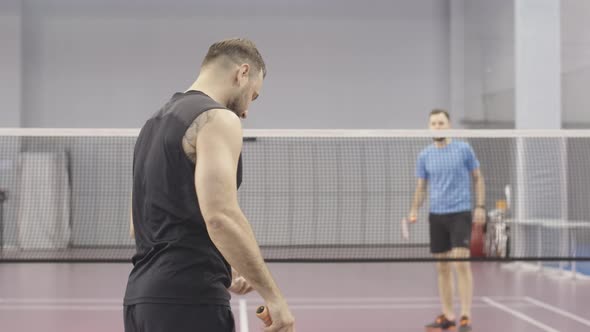 Back View of Tattooed Caucasian Sportsman Competing in Badminton with Young Blurred Man at the alt