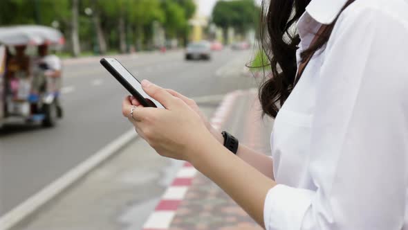 Young woman typing a message on a smartphone while standing beside the street in Bangkok Thailand.