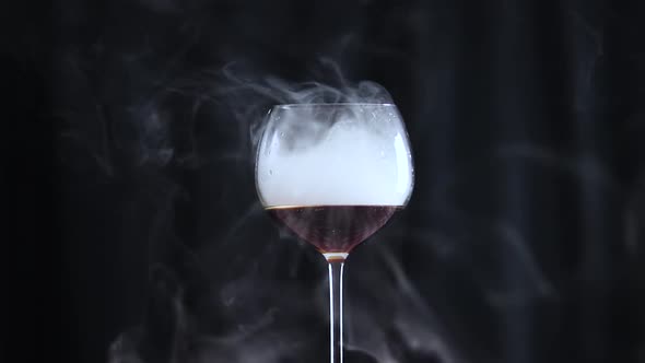 Glass Filled with a Dark Drink and Smoke with a Black Background alt