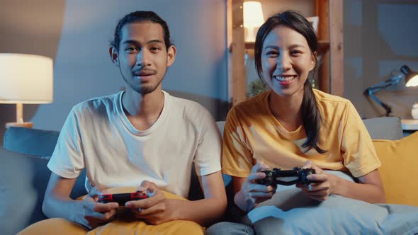 Happy asia young couple man and woman sit couch use joystick controller play video game.