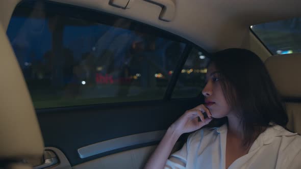 young Asia businesswoman looking out of window car while sit on passenger back seat in urban city. alt