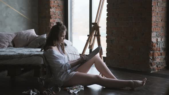 Portrait Artist at Work. Girl Paints a Picture of Sitting on the Floor in the Home Studio alt