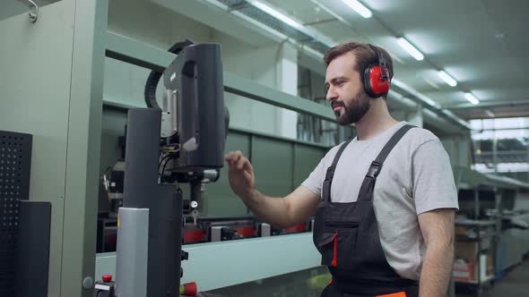 Portrait of Adult Employee Man 30s Wearing Working Overall and Headphones Touching with Equipment alt