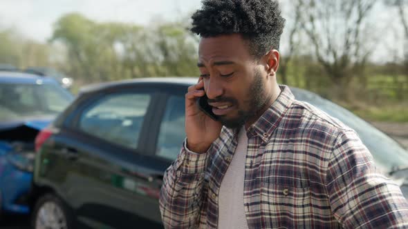 Young man standing by damaged car after traffic accident reporting incident