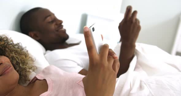 Happy couple using mobile phone on bed alt
