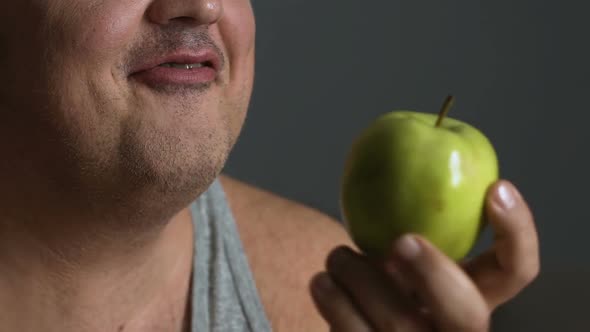 Overweight Man Biting Fresh Apple, Keeping to A Healthy Diet to Lose Weight alt
