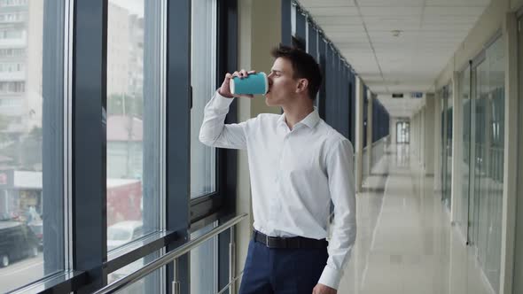 Thoughtful Businessman Looks Out the Window in Office and Drinks a Cup of Coffee alt