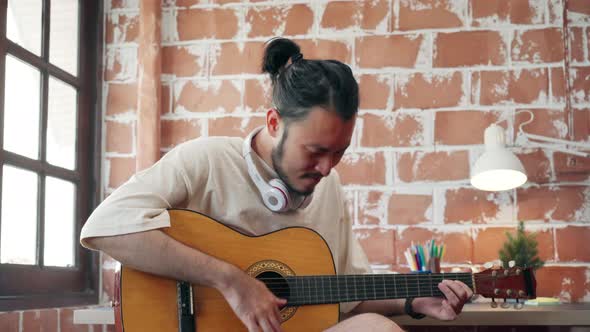 Asian man designer working home using laptop in living playing guitar and singing in living room. alt