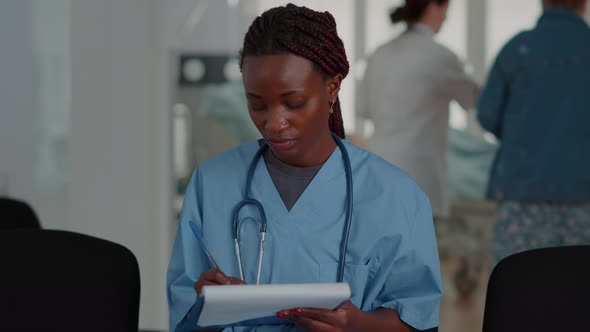 Close Up of African American Nurse Looking at Checkup Files in Waiting Room alt