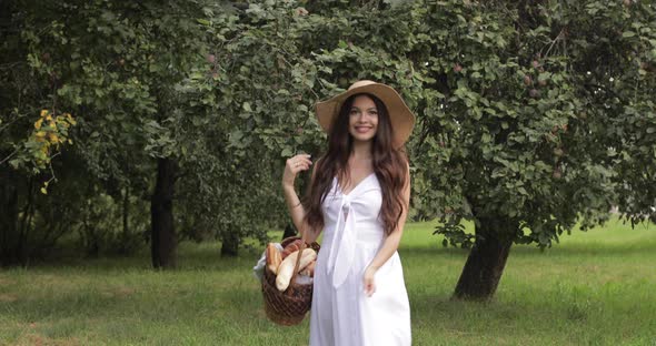 Young Beautiful Woman Walks Through the Garden with a Basket in Her Hands and Smiles