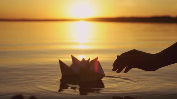 Human Hand is Launching Handmade Paper Boats Into the Lake at Sunset alt