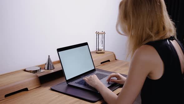 A Woman in a Home Office Sitting at a Table Types Text on a Laptop alt