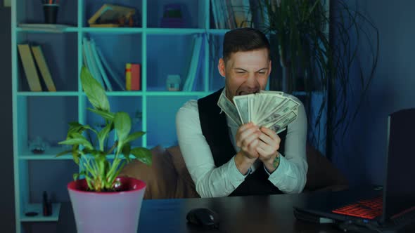 Young Man Counts Money Sitting in Armchair Before Computer in Office alt