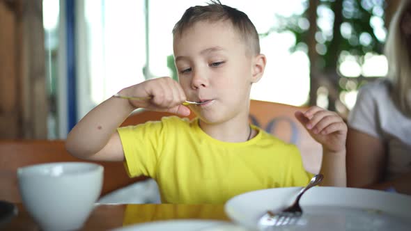 Little Boy Eats a Pancake with Sour Cream in a Cafe in the Morning for Breakfast alt