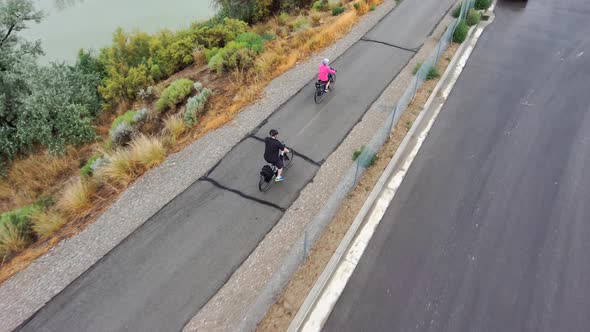 Senior couple ride on a riverside path together for exercise and bonding - aerial view alt