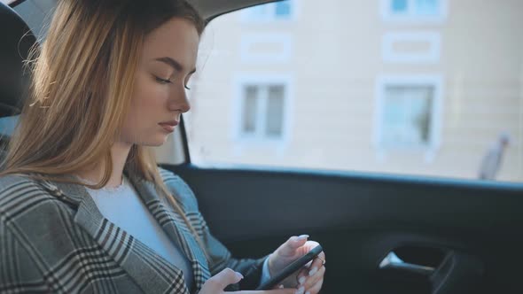 A Young Girl Rides in the Backseat of a Car and Watches Her Smartphone alt