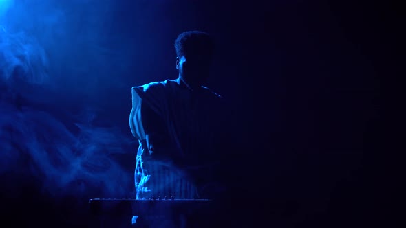 Silhouette of African American Man Playing Piano Synthesizer on Stage in Dark Smoky Studio alt