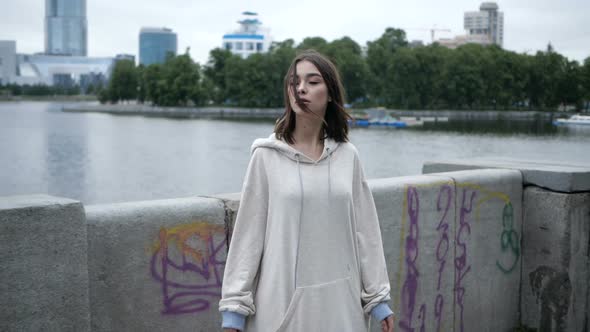 A Girl in a White Hoodie Walks Along the River Embankment